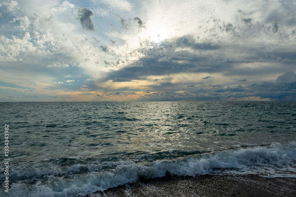The sound of sea waves crashing on a pebble beach. The setting sun hid behind dark clouds. The sound of sea waves crashing on a pebble beach. The setting sun hid behind dark clouds.