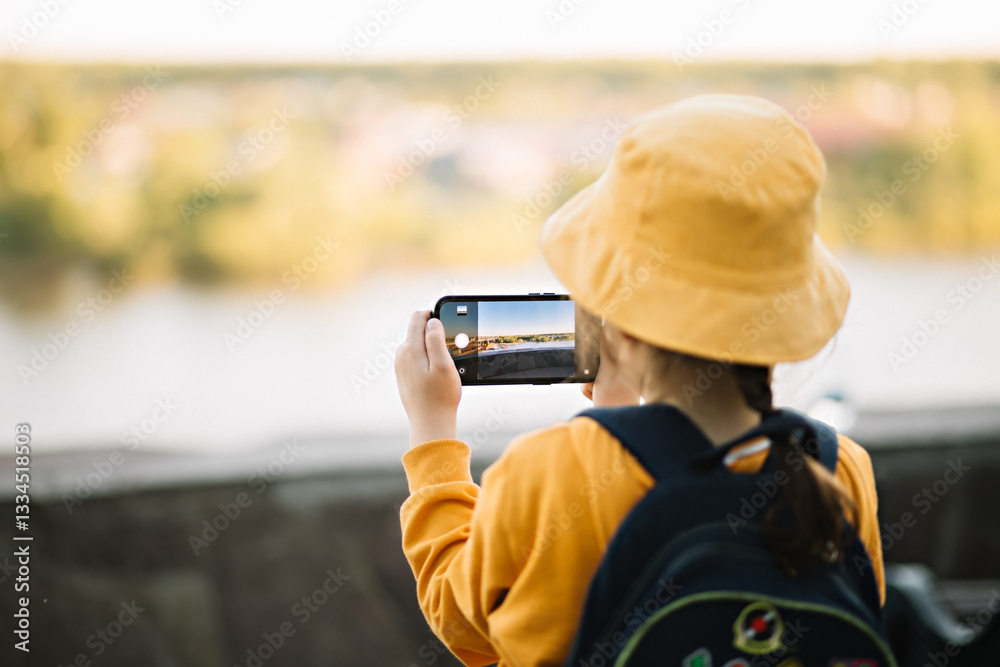 Obraz premium Cute little girl taking selfie with mobile phone looking at camera in a park. Kid blogger recording video vlog.