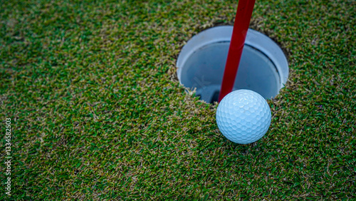 Golf ball on golf course near hole with flagstick in morning sunshine.