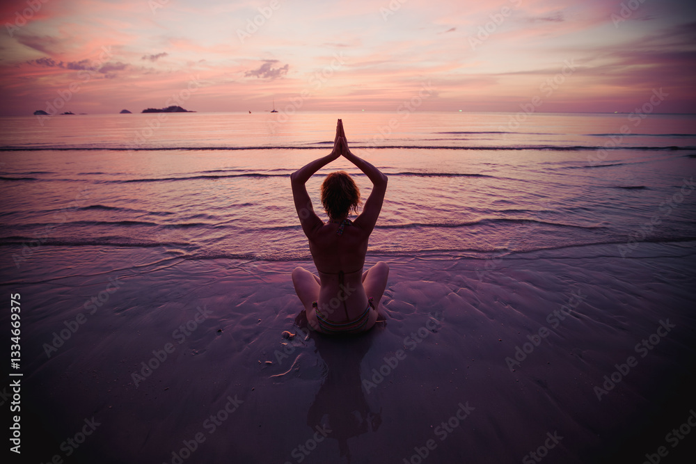 A woman sits in the lotus position, meditating during a serene sunset at the water's edge, blending tranquility and natural beauty.
