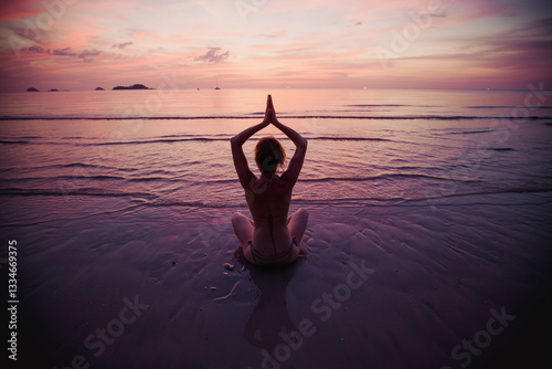 Obraz na płótnie A woman sits in the lotus position, meditating during a serene sunset at the water's edge, blending tranquility and natural beauty. w salonie