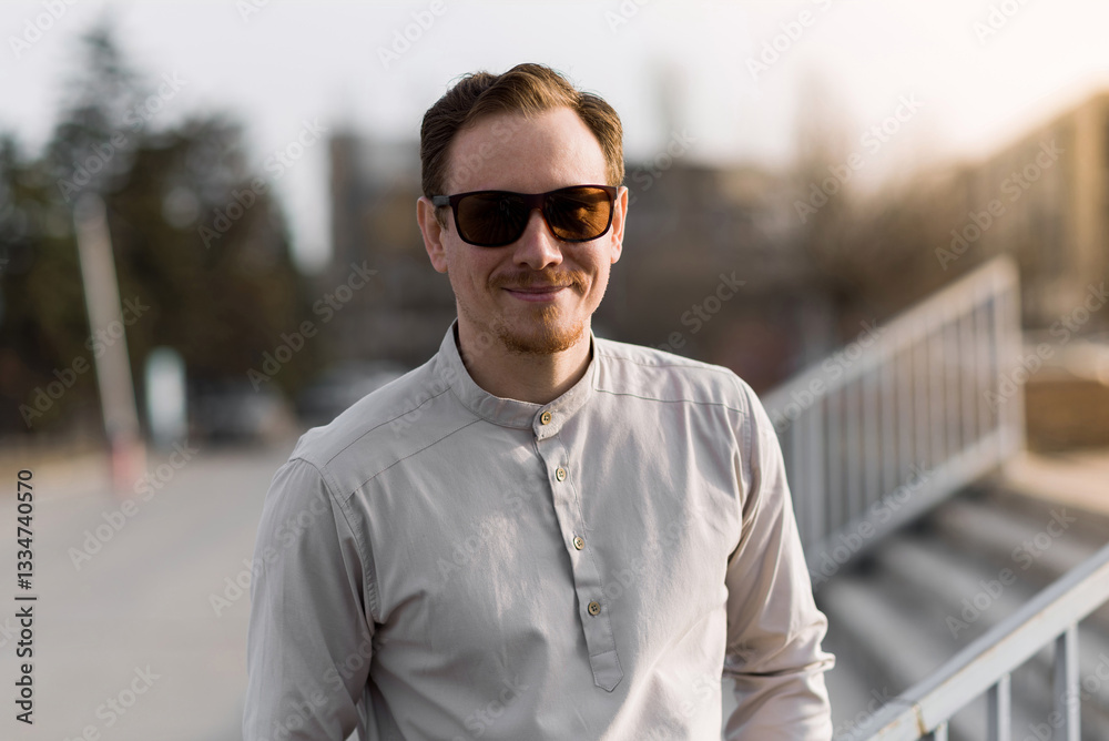 Portrait of an attractive redhead young man wearing stylish clothes and sunglasses. The man smiles and looks at the camera. Walking on the street on a sunny spring or autumn day. Portrait of an attractive redhead young man wearing stylish clothes and sunglasses. The man smiles and looks at the camera. Walking on the street on a sunny spring or autumn day.