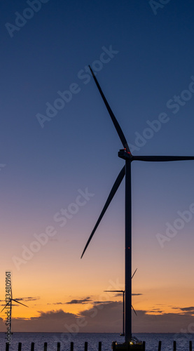a single offshore wind turbine stands in the sea against blue orange sky in Netherlands