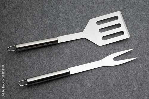 , Deutschland, 15.03.2025,  Hochwertiges Edelstahl-Grillbesteck, bestehend aus Grillzange, Grillgabel und Grillwender, auf grauem Hintergrund. Perfekt für BBQ und Grillfans.