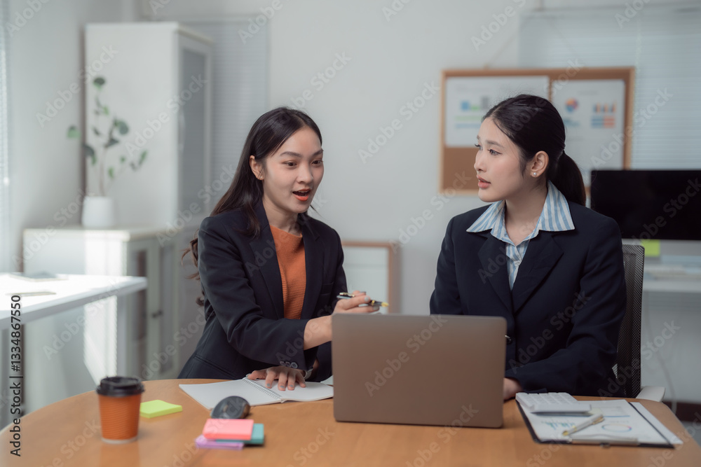 Two asian businesswomen are discussing work using laptop and documents in the office, they are pointing at the laptop screen and talking about the project Two asian businesswomen are discussing work using laptop and documents in the office, they are pointing at the laptop screen and talking about the project