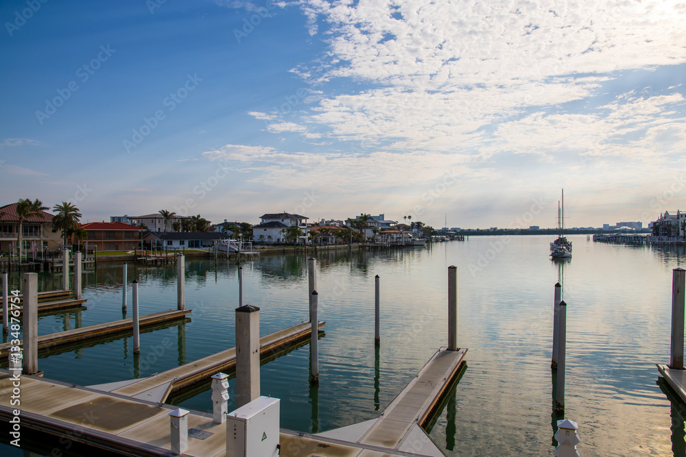 Fototapeta premium A gorgeous landscape with ocean water, homes and boats on the water, blue sky and clouds, lush green palm trees at sunrise in Clearwater Florida USA