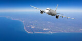 White passenger airplane flying over coastal area on sunny day