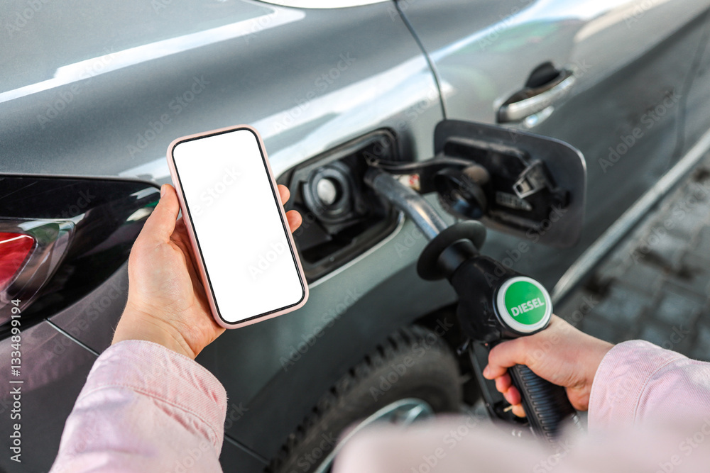 Person refueling a car with diesel pump while holding a smartphone with blank screen. Concept of refueling, transport, diesel fuel, gas station, mobile app, and payment