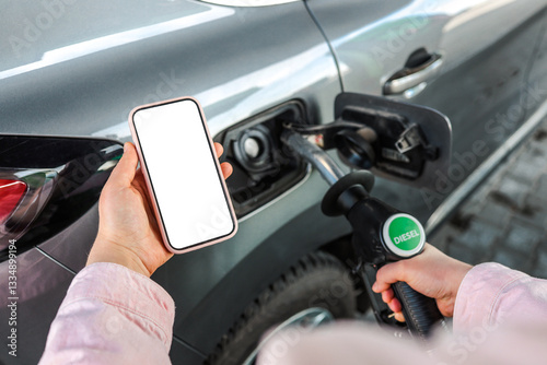 Obraz na płótnie Person refueling a car with diesel pump while holding a smartphone with blank screen. Concept of refueling, transport, diesel fuel, gas station, mobile app, and payment w salonie