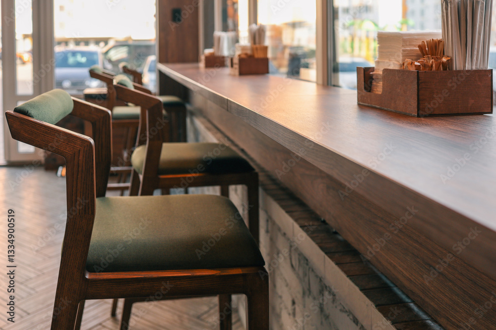 Cozy modern cafe interior with wooden chairs and high counter along the window. Warm sunlight creates a welcoming atmosphere. Minimalist design with natural wood and neutral tones Cozy modern cafe interior with wooden chairs and high counter along the window. Warm sunlight creates a welcoming atmosphere. Minimalist design with natural wood and neutral tones