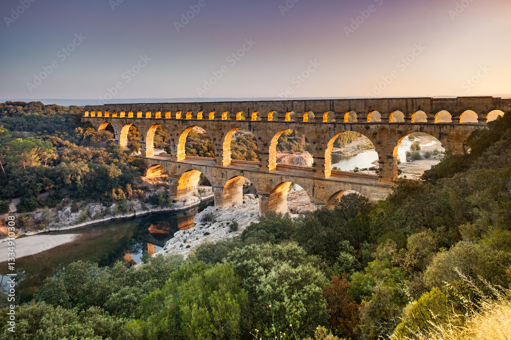 Obraz premium Pont du Gard, ancient Roman aqueduct bridge, elevated view, river bend and complete arches, early morning golden light, Gorges du Gardon, natural landscape, UNESCO Biosphere Reserve, Provence, France