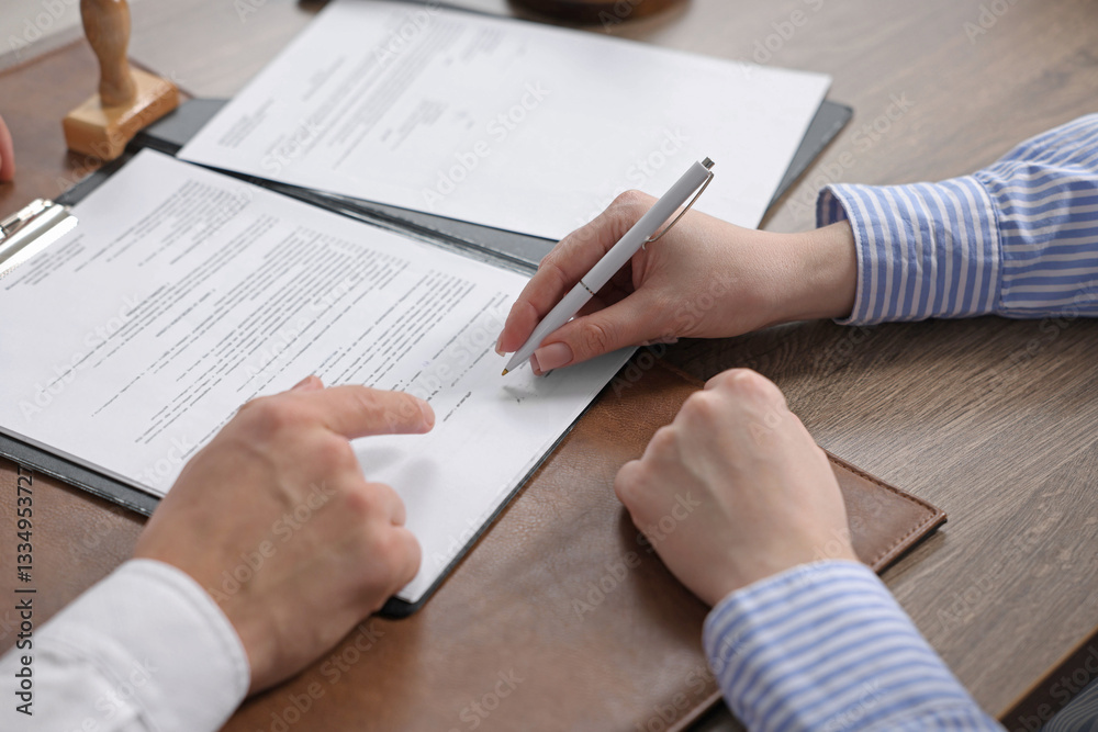 Notary pointing at document and client putting signature at wooden table indoors, closeup Notary pointing at document and client putting signature at wooden table indoors, closeup