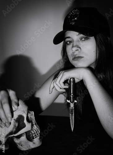 A pretty girl in a black cap with a stiletto in her hand. Black and white art photo.