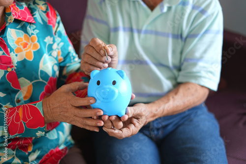 Saving money investment for future. Senior asian man hands putting money coin in piggy bank. Old man plans to start saving money and retirement budget and to buy life insurance and health insurance.
