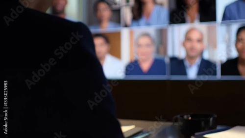 Silhouetted business professional participating in a virtual video conference with multiple colleagues displayed on a large screen. Concept of remote work and digital communication