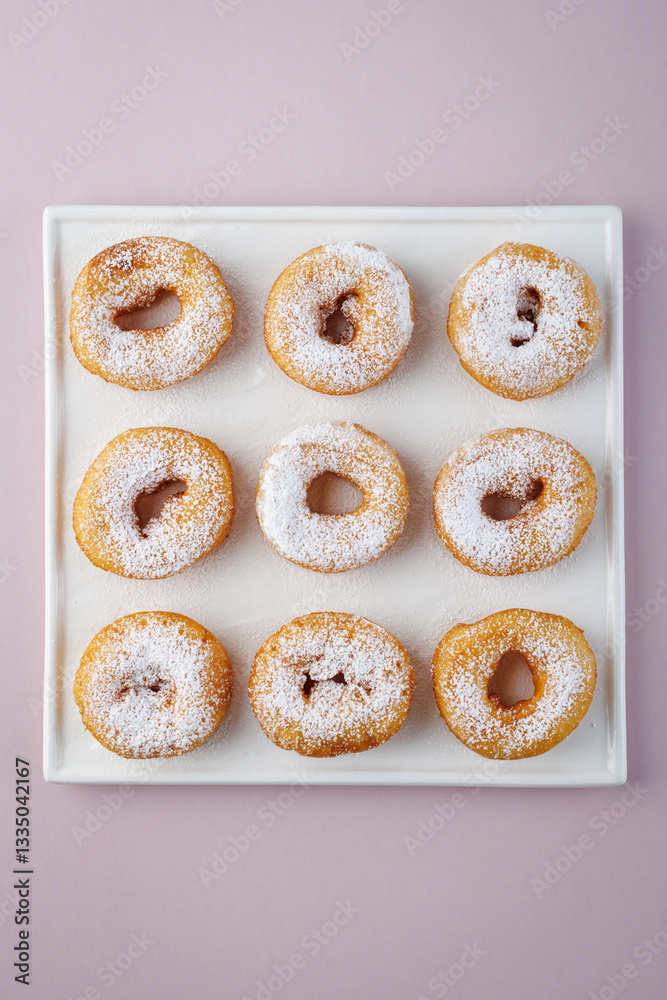 Donuts with powdered sugar on a light plate and a delicate purple background. Top view