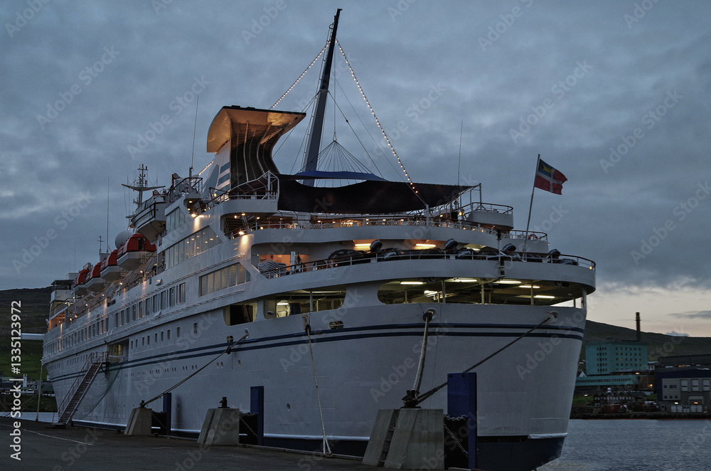 Classic expedition cruiseship cruise ship liner Delphin docked at pier in Thorshavn, Faroe Islands with cliffs and fjord landscape in background and city skyline during Arctic Circle summer cruising