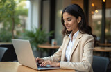 Smiling indian businesswoman types on laptop at office eatery. Corporate employee works, types on notebook. Freelancer works with wireless technology. Happy expression, confidence, success at work.