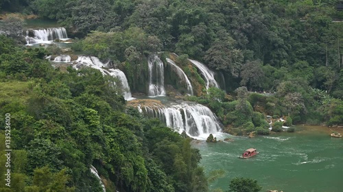Lush vegetation surrounds the multi tiered Ban Gioc (Detian) Falls, where tourist boats navigate the turquoise waters