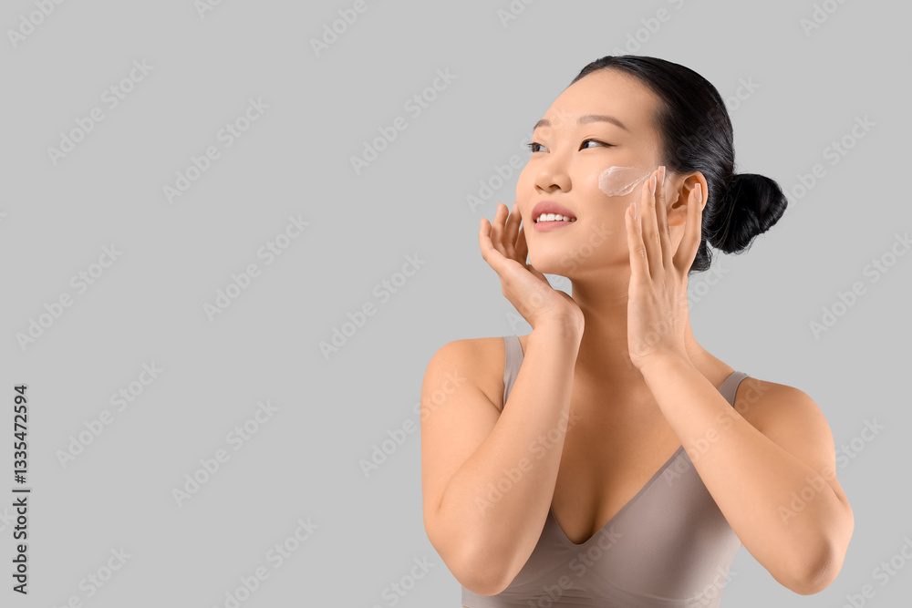 Young Asian woman applying facial cream on grey background Young Asian woman applying facial cream on grey background