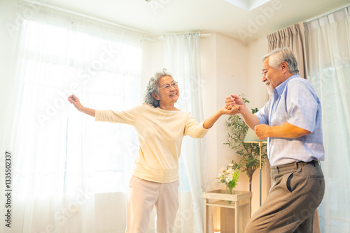 Happy Asian family senior couple enjoy and fun leisure activity lifestyle dancing together in living room. Healthy elderly husband and wife relaxing at home. Aged people mental healthcare concept.