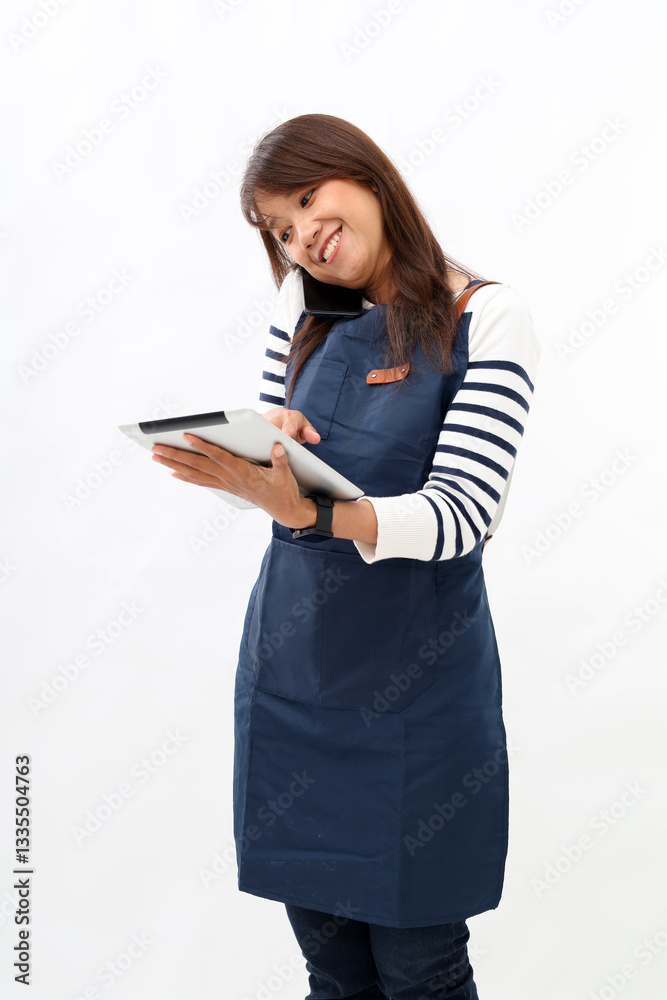 Young asian woman barista employee wear blue apron work in coffee shop use tablet pc computer speak by mobile cell phone isolated on white background Small business startup Young asian woman barista employee wear blue apron work in coffee shop use tablet pc computer speak by mobile cell phone isolated on white background Small business startup