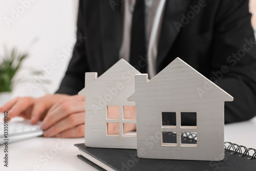 Real estate agent with calculator at white table in office, focus on house figures and notepad. Home appraisal