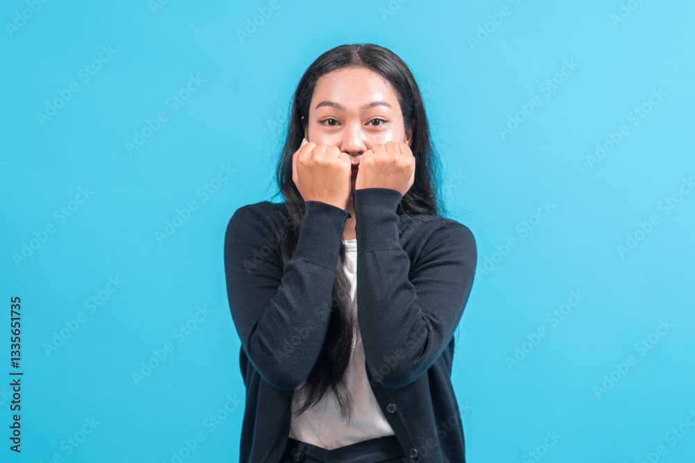 Asian woman with long black hair wearing a black cardigan and white shirt, standing against a blue background, raising both fists near her face with an excited and cheerful expression. Asian woman with long black hair wearing a black cardigan and white shirt, standing against a blue background, raising both fists near her face with an excited and cheerful expression.