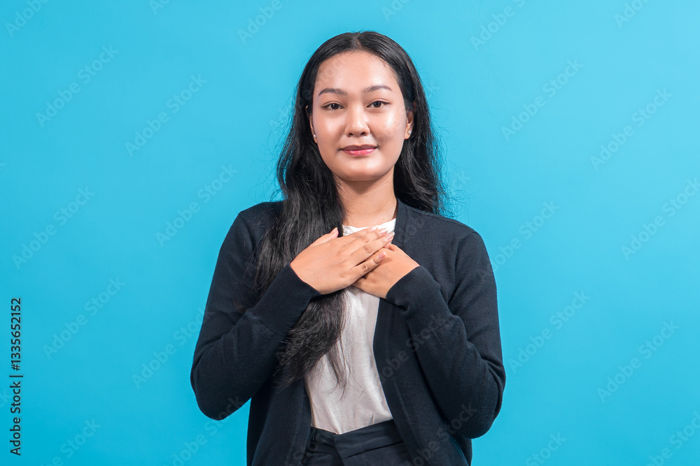 Asian woman with long black hair wearing a black cardigan and white shirt, standing against a blue background, gently placing both hands on her chest with a grateful and warm expression. Asian woman with long black hair wearing a black cardigan and white shirt, standing against a blue background, gently placing both hands on her chest with a grateful and warm expression.
