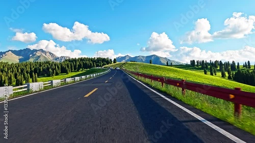 Asphalt road through vibrant green hills towards mountains under blue sky