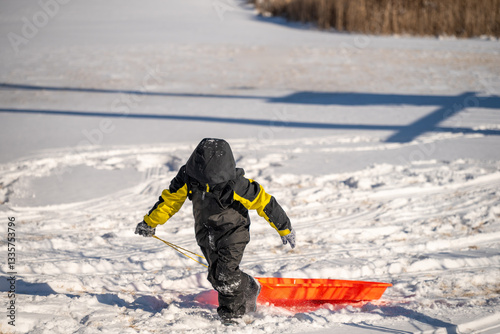Child pulling a sled up a snow covered hill covered with tracks