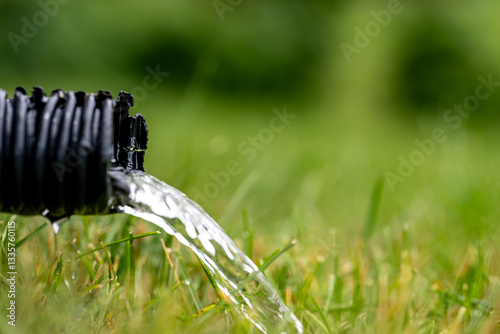 Residential sump pump drain line discharging water into grass yard after a rainstorm 