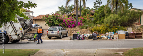 A large garbage truck collecting large bulky waste items from a suburban street.