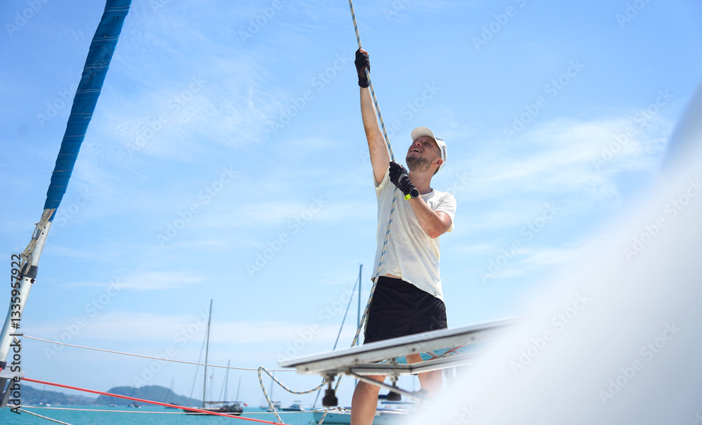 Male captain on deck of sailboat opening sails pulling the rope