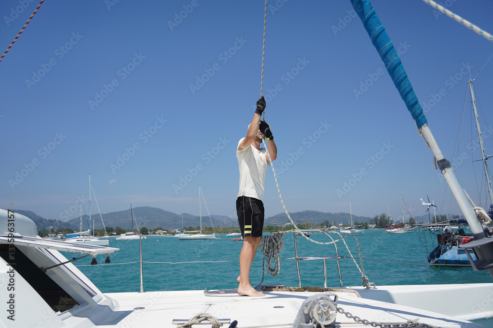 Naklejka premium Male captain on deck of sailboat opening sails pulling the rope