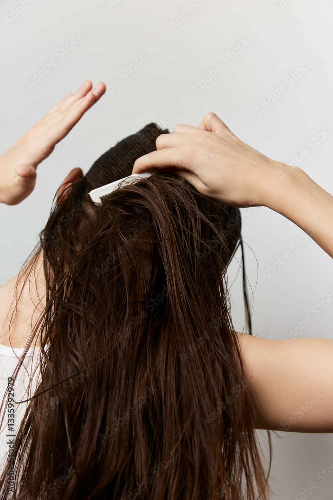 Fototapeta premium hair care, hairstyle, grooming, beauty, personal care A woman with long, wet hair is styling her hair using a hair comb against a neutral light background, emphasizing self care and personal grooming