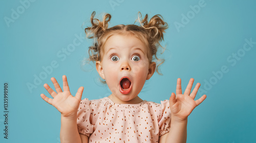 Portrait of a surprised cute little toddler girl child over a pink background, looking at the camera, pointing hands to the left side. Advertising children's products.