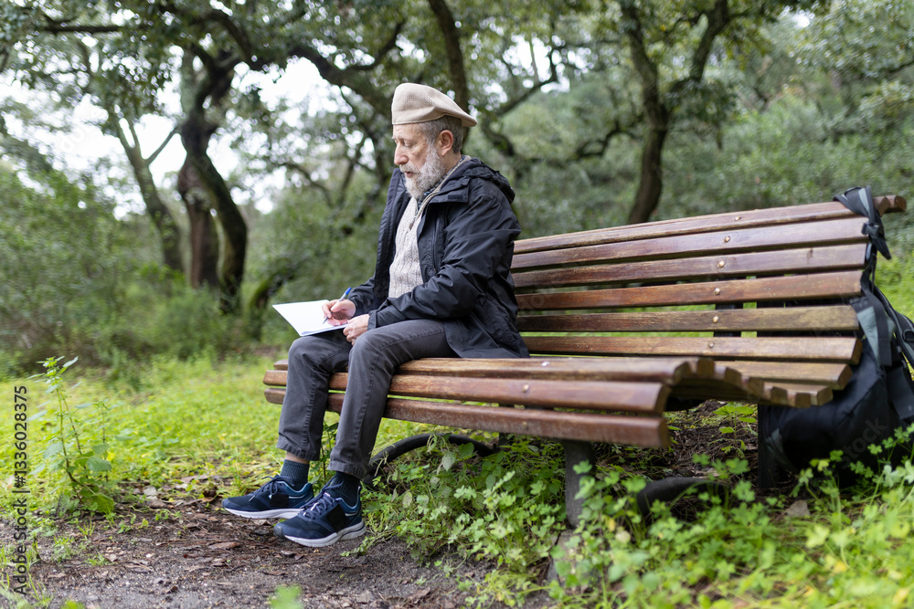 Senior man writing on notepad while sitting on bench in park Senior man writing on notepad while sitting on bench in park