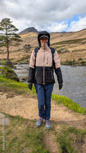 Beautiful woman backpacker in hooded jacket hiking at river Erriff near Aesleagh, county Mayo, Ireland, Irish landscape, mountains and nature background	 photo