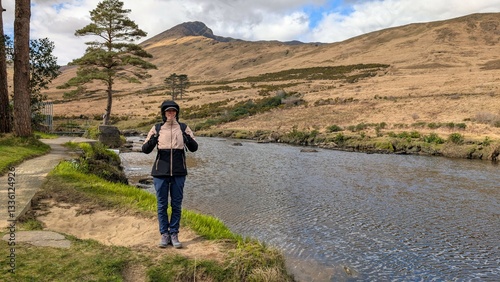 Obraz na płótnie Beautiful woman backpacker in hooded jacket hiking at river Erriff near Aesleagh, county Mayo, Ireland, Irish landscape, mountains and nature background w salonie