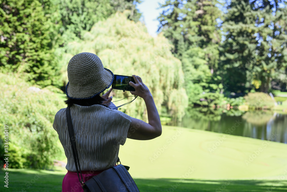 Woman taking photos of trees and lakes in a park using a smartphone. Seattle. USA.