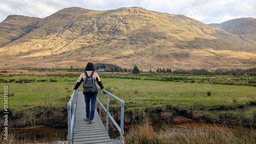 Beautiful woman backpacker in hooded jacket hiking at river Erriff near Aesleagh, county Mayo, Ireland, Irish landscape, mountains and nature background	