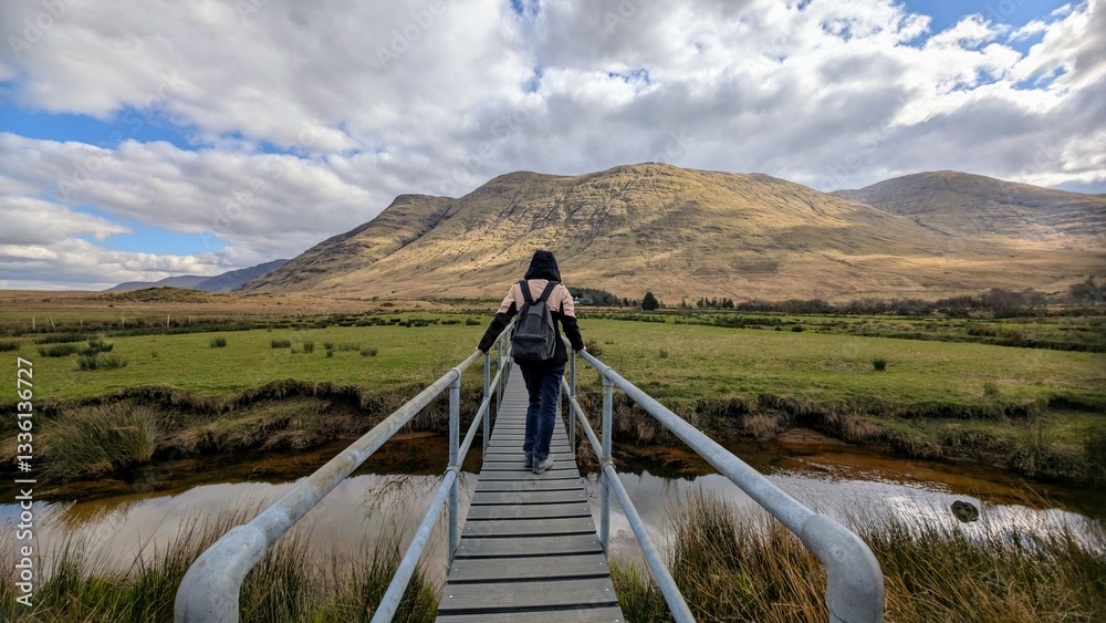 Beautiful woman backpacker in hooded jacket hiking at river Erriff near Aesleagh, county Mayo, Ireland, Irish landscape, mountains and nature background