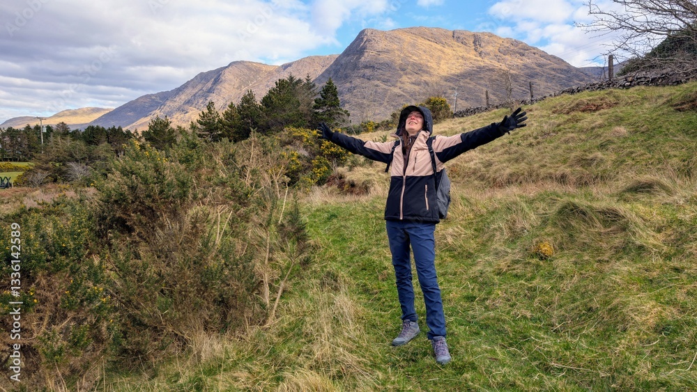 Beautiful woman backpacker in hooded jacket hiking at river Erriff near Aesleagh, county Mayo, Ireland, Irish landscape, mountains and nature background