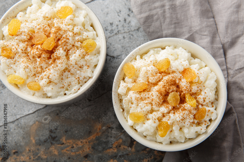 Classic Milk Rice Pudding with Cinnamon and Golden Raisins on Top Close-up in Ramekin on Table. Horizontal top view from above