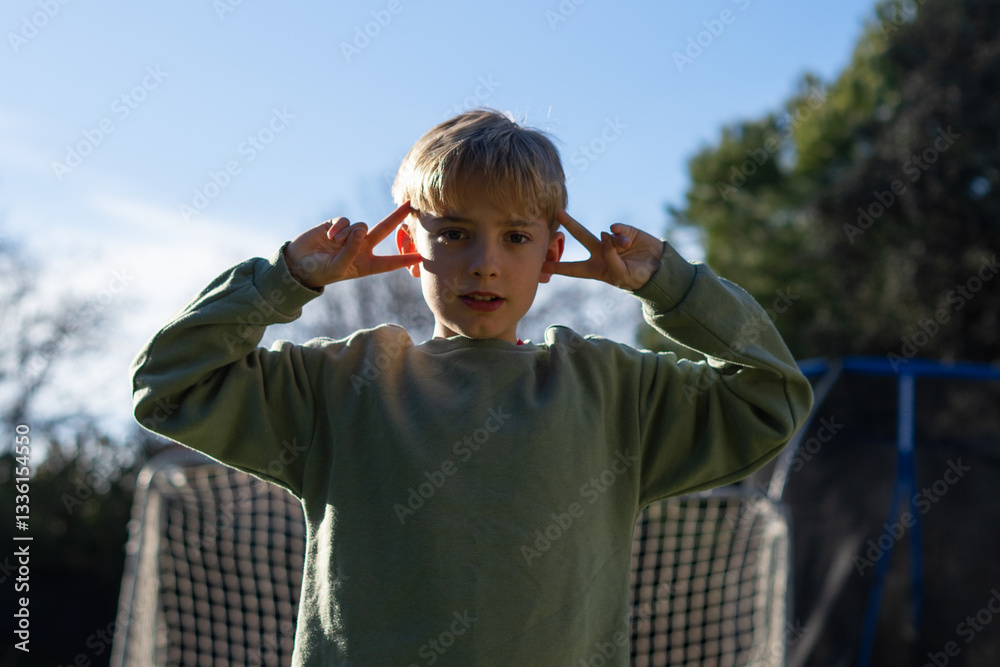 Naklejka premium Young boy making peace sign with fingers on head in garden