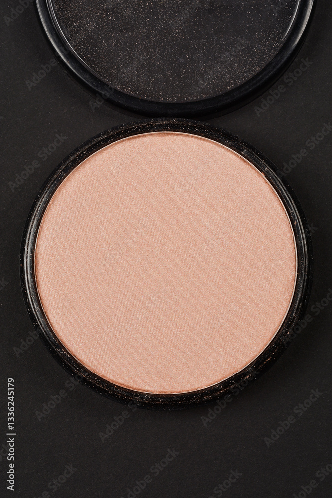 A close-up shot of a single, round, powder pan from a makeup palette, set against a black background A close-up shot of a single, round, powder pan from a makeup palette, set against a black background