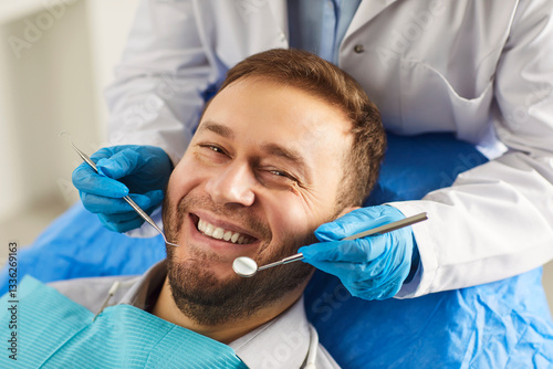 Happy man smiling toothily while being on medical check up in dentistry clinic, undergoes orthodontic dental services, taking care of teeth hygiene, having perfect smile after whitening