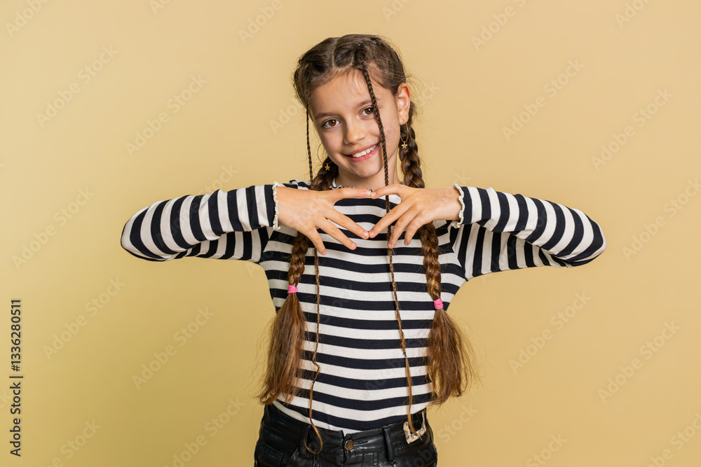 Fototapeta premium Girl in love. Smiling attractive young preteen child kid makes heart gesture demonstrates love sign expresses good positive feelings and sympathy. Teenager children isolated on beige background