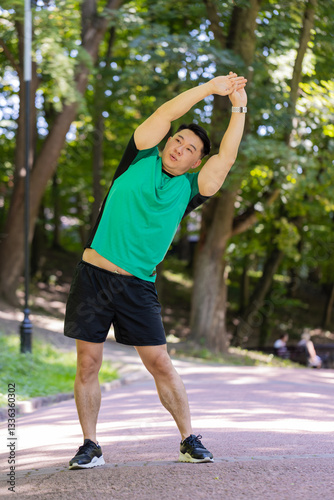 Asian young man sportsman male athletic trainer in good physical shape doing warm-up morning sport exercises, yoga gymnastic knead neck stretching muscles avoid body tension healthy lifestyle in park.